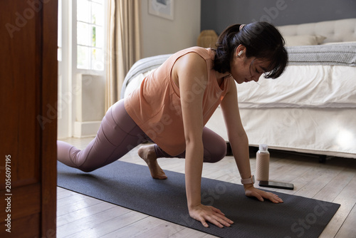 Black yoga mat resting beside water bottle on wooden floor by bed in softly lit bedroom
