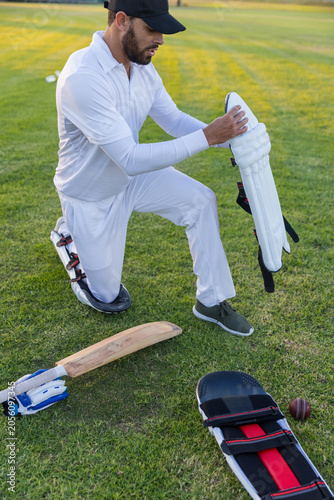 Cricket equipment lying on trimmed cricket field, bat, gloves, pads and leather ball