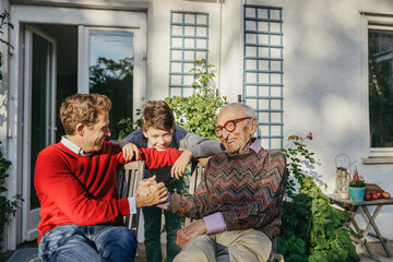 Smiling man holding hand of father by son in backyard