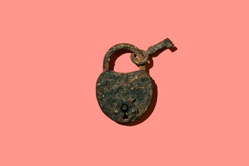Old rusty heart shaped padlock with key on pink background