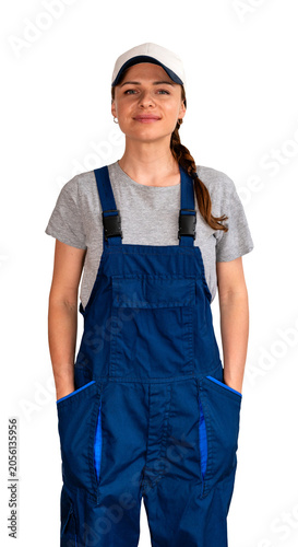 Adult female blue-collar worker wearing blue bib overalls and cap standing with hands in pockets.
