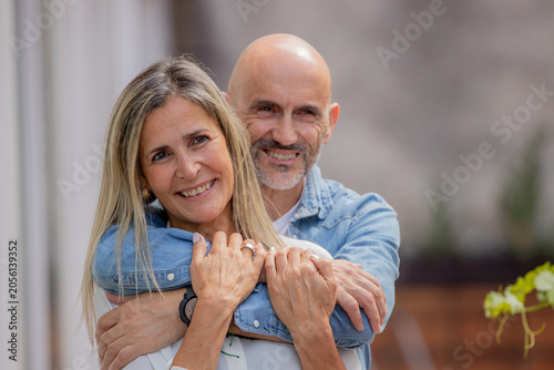Happy hispanic couple embracing outdoors, smiling woman with blonde hair and bald man in casual denim, sharing a tender moment