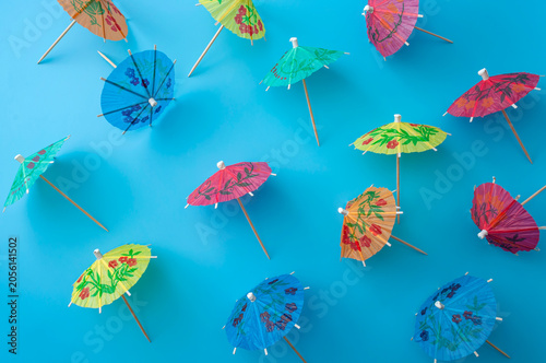 Colorful paper cocktail umbrellas scattered on a bright blue background, top view flat lay. Summer, tropical vacation and cocktail party celebration concept design with vibrant colors