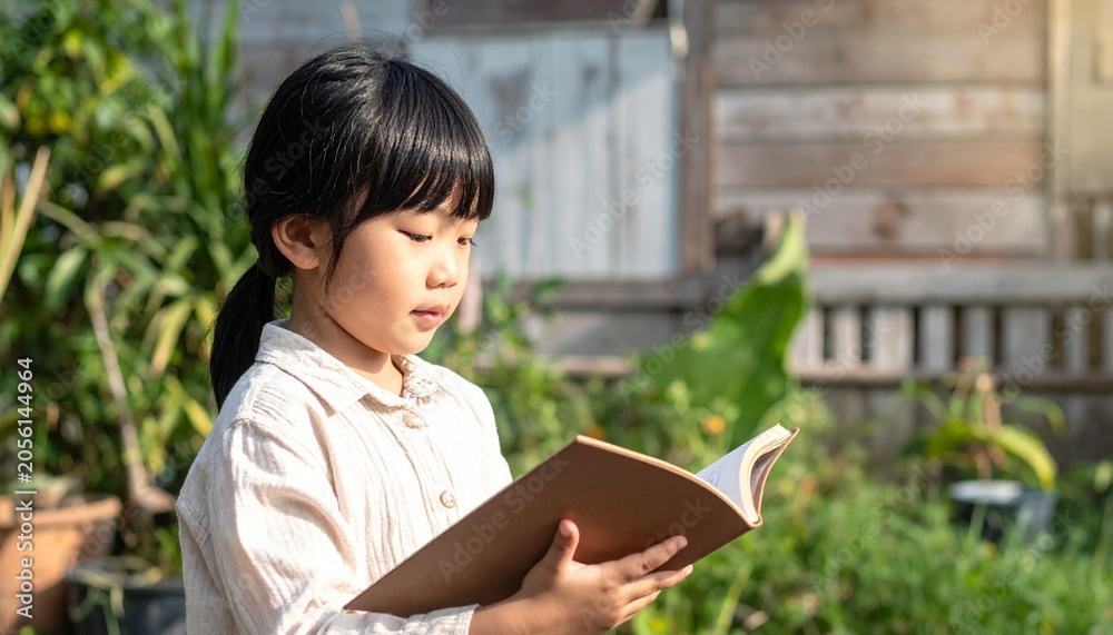 Fototapeta premium Young girl in light shirt reading a book outdoors