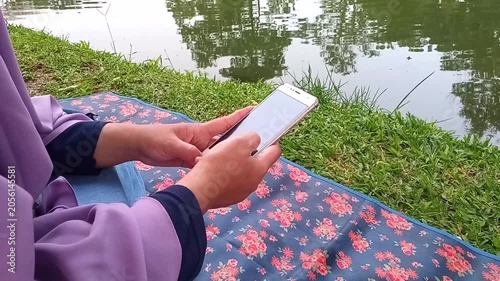 Faceless person swiping smartphone by calm lake side outdoors