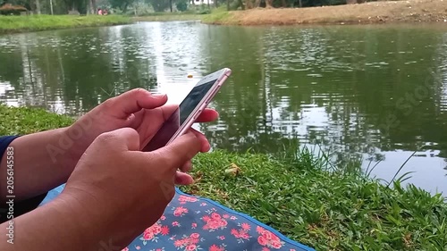 Faceless person swiping smartphone by calm lake side outdoors