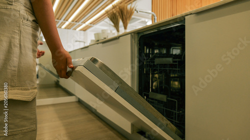 Photos Person opening a modern built-in dishwasher in a clean kitchen setting