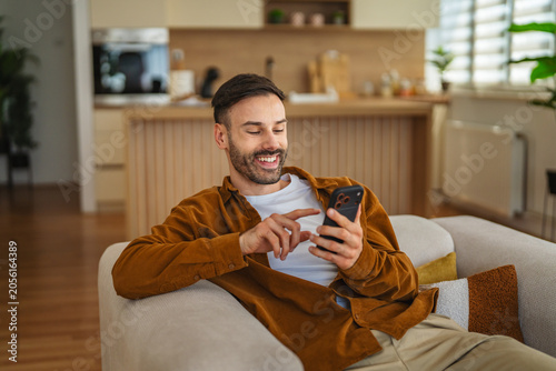Obraz na plátně Smiling man relaxing on sofa using smart phone
