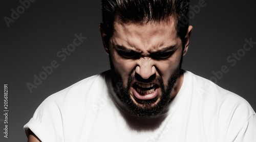 Bearded man yells with intense anger. Face contorted in rage shows teeth. Human emotion captured in dramatic portrait. Negative feeling expressed strongly.