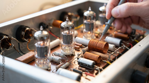 Technician repairing vintage electronic device with vacuum tubes using an oscilloscope probe. 