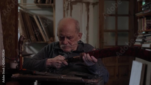 Elderly craftsman working in his old workshop, carefully restoring collectible Japanese bladed weapons