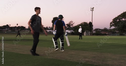 Teenage bowler bowling ball on pitch, batsman calling single, batting partners switching ends