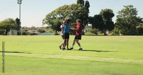 Friends hugging and approaching on grassy sports field, with shin guards and blue baseball cap