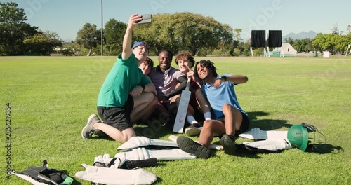 Five cricket teammates snapping selfie with smartphone on cricket field, showing bat and pads