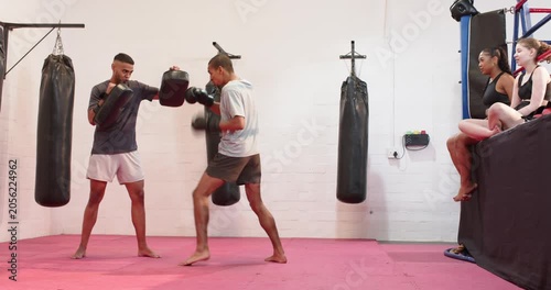 Trainee executing combos in martial arts gym with trainer raising focus pads for training