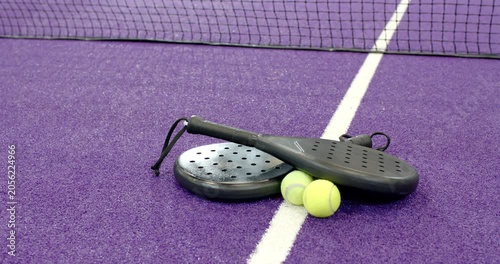 Camera starting overhead and capturing padel rackets and tennis balls resting by net on purple turf