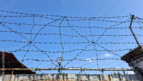 Tableau sur toile Barbed Wire Fence Against Blue Sky Security Barrier Protection and Restricted Ar