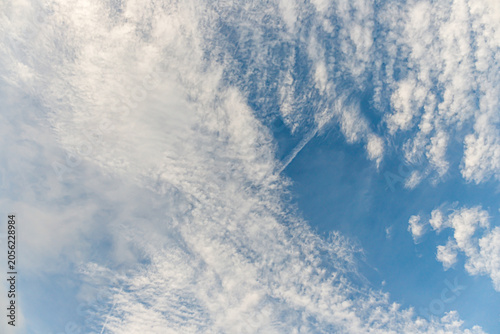 Bild auf Leinwand Bright clouds in a blue sky with a few trails from planes visible above during d