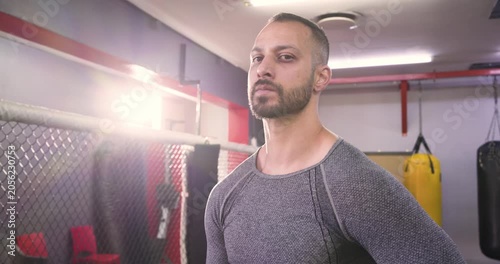 Adult indian boxer wearing boxing gloves catching breath after sparring shifting gaze in cage