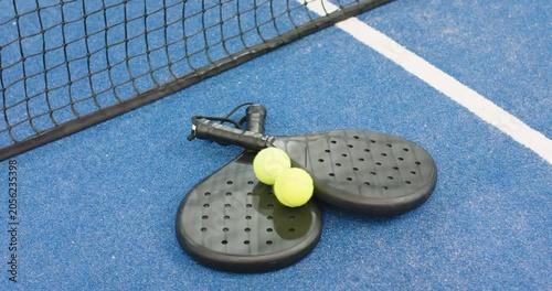 At start padel rackets, balls are resting on blue court at net awaiting match start
