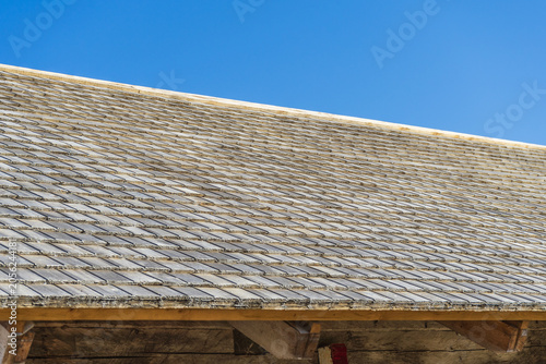 Rustic cedar shake roof texture background with repeating pattern of old wooden tiles. Detailed texture of traditional weathered wooden shingle roof against clear blue sky.