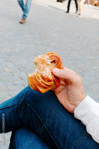 a man holds a bitten kanelbulle in a public square