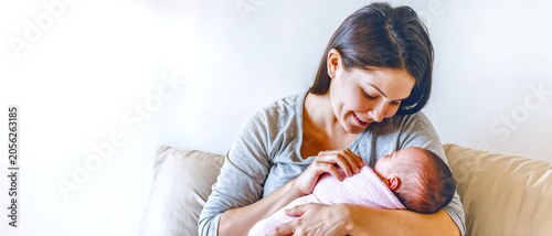 A loving Caucasian mother smiling down at her newborn baby, cradling the infant wrapped in a soft pink blanket, captured in a serene and cozy home environment.
