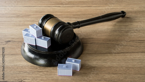 Wooden legal gavel and sound block placed next to miniature shipping containers on a wooden desk illustrating maritime law and trade regulations.