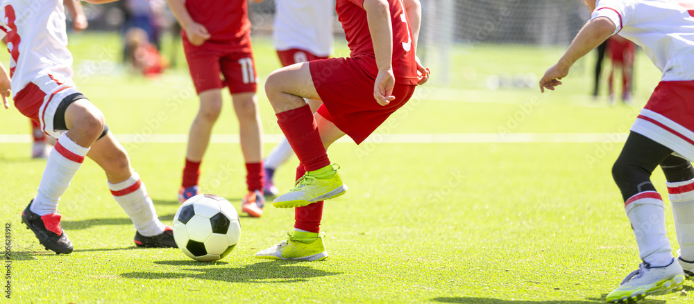 Naklejka premium Football Game For Children; Youth Soccer Action: Close-Up of Kids Legs Kicking Ball During Football Match