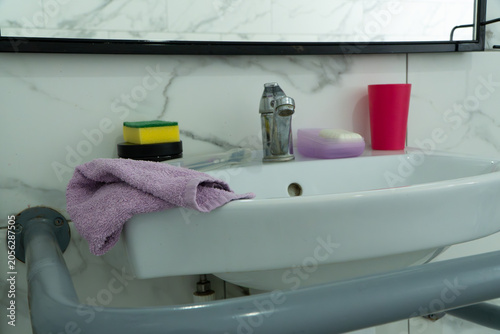 Foto A close-up shot shows a white ceramic washbasin equipped with a grey safety support handrail for disabled people in a modern tiled bathroom