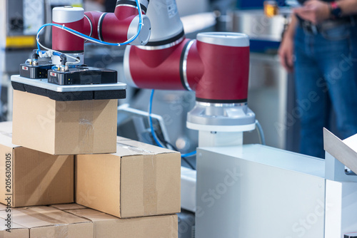 Collaborative robotic arm lifting cardboard boxes in an automated warehouse, showcasing smart manufacturing, industrial automation, logistics, packaging, and Industry 4.0 technology