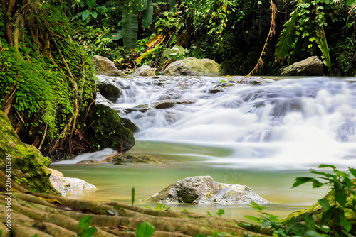 Tropical waterfall flowing through lush rainforest jungle with moss-covered rocks, 