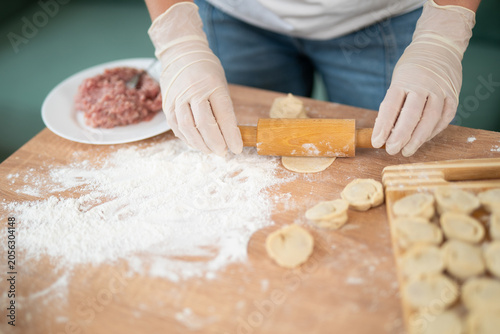 Fotografie Woman in gloves using rolling pin to flatten dough for handmade dumplings