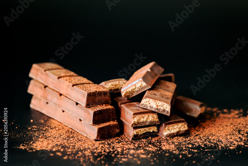 Photos Stacked chocolate wafer bars with cocoa powder on dark background