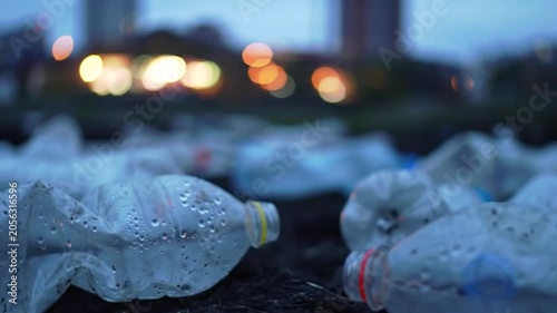 Discarded plastic water bottles littering ground in urban park at twilight with city lights