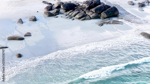 Eine beeindruckende Luftansicht vom Plage de Boutrouilles, bei der sanfte, weiße Wellenmuster auf den hellen Sandstrand und die charakteristischen, dunklen Felsformationen treffen.