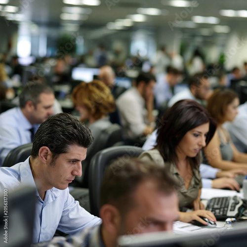 Employees working at computers in a busy open-plan office. Modern workplace environment with focus, teamwork, and daily business operations.