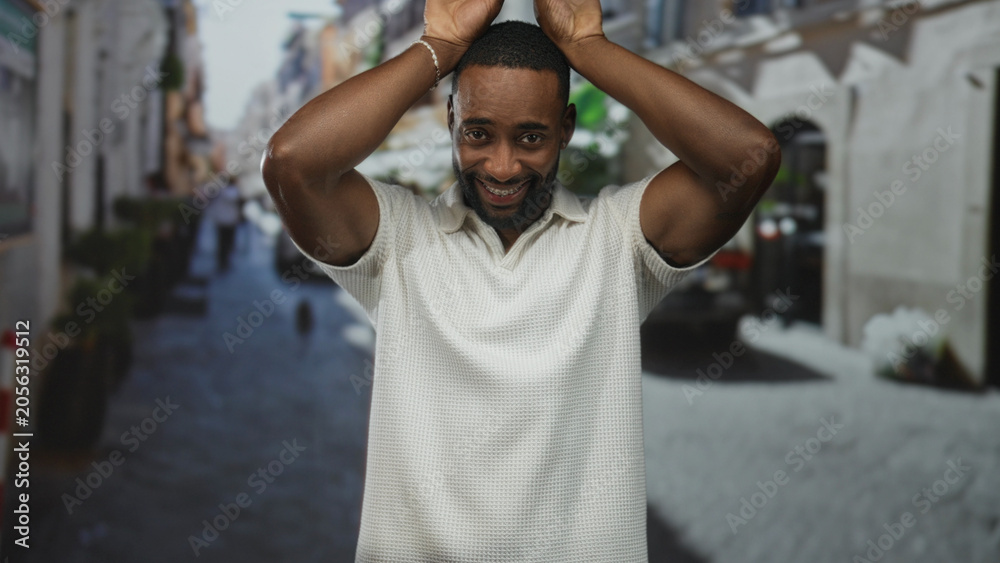 Naklejka premium Man with hands above head and palms raised on street wearing white polo shirt, smiling toward camera; playful moment.