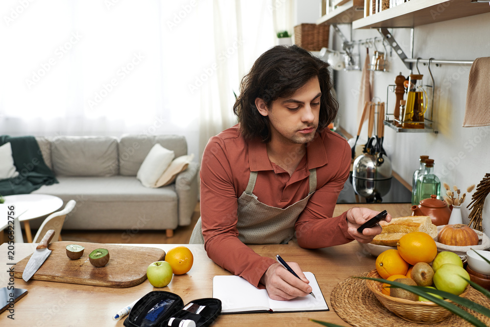 Fototapeta premium A young man with diabetes records his daily routine while preparing healthy snacks at home.