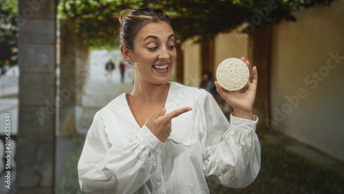 Foto Woman in white blouse points finger to ricecake held at eye level in street archway; healthy snack joy