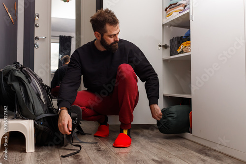 Fotografie Young bearded man packing sleeping bag or gear into wardrobe before travel