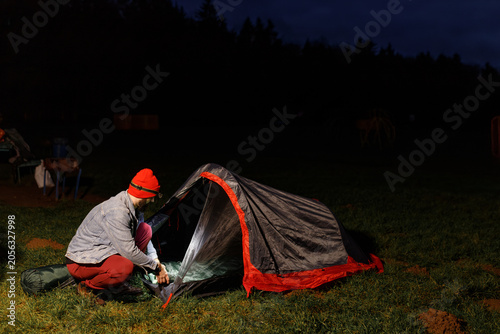 Canvastavla Young bearded father and little son pitching tourist camping tent fixing peg into ground on lake shore at dark twilight night