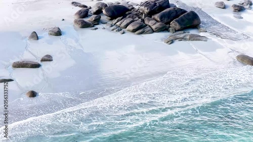 Eine beeindruckende Luftansicht vom Plage de Boutrouilles, bei der sanfte, weiße Wellenmuster auf den hellen Sandstrand und die charakteristischen, dunklen Felsformationen treffen.