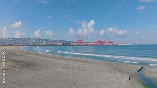 High angle view of the new Bay Port in Haifa, Israel, featuring red industrial cargo cranes alongside beautiful turquoise Mediterranean sea water and city coastline.