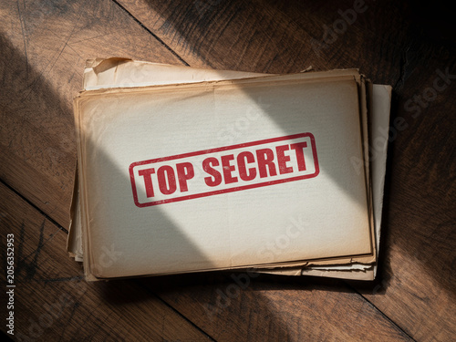 Confidential files stack with red top secret stamp on dark wooden table