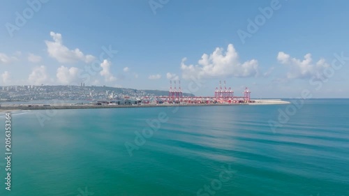 High angle view of the new Bay Port in Haifa, Israel, featuring red industrial cargo cranes alongside beautiful turquoise Mediterranean sea water and city coastline.