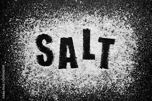 Word salt stenciled in white sea mineral powder on black background representing essential culinary ingredient