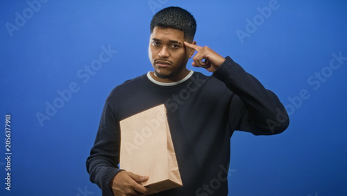 Photos Man holding a paper bag with finger to temple and furrowed brow in studio, facing an apparent delivery mixup and order delay; frustration
