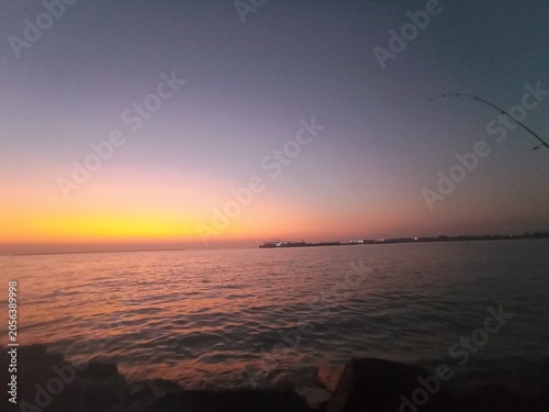 A stunning sunrise over a rustic wooden pier, featuring a vibrant sky painted in shades of orange, pink, and purple. The calm ocean waters perfectly reflect the warm gradient of the dawn, creating a p