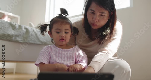Asian Mother and Two Year Old Toddler Girl using Tablet on Floor Together morning light	